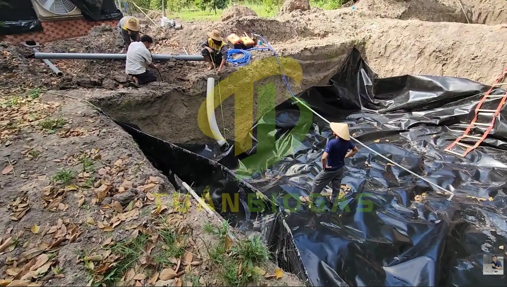 Đội ngũ công nhân trang trại kéo mép bạt túi biogas tròn lên thành bờ hố đất