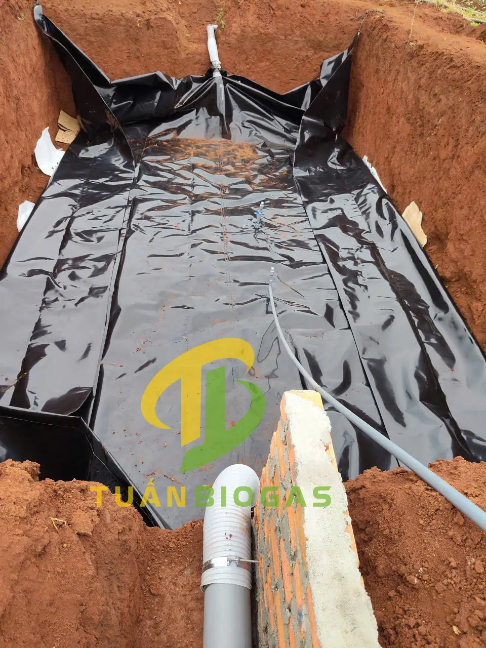 Kỹ thuật viên trải túi biogas tròn xuống đáy hố đất và kéo ống PVC 34 lên bờ